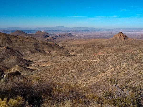 A trail descends a desert mountain slope, offering views of the surrounding mountains and plateaus.