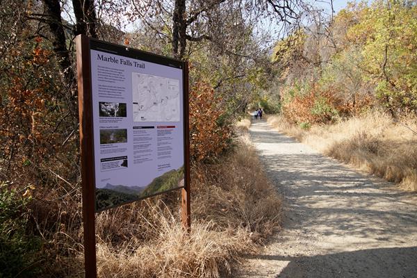 A blue metal panel sits in a metal frame next to a trail behind it are yellow grass and oak tree