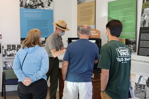 A ranger in a flat hat presents information to three visitors.