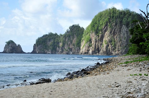 Outdoors; landscape view of sandy beach foreground, blue waters, and steep cliffs in background.