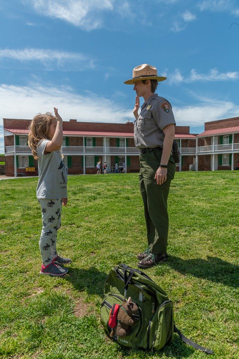 A ranger and child stand facing each other; both have their right hand in the air.