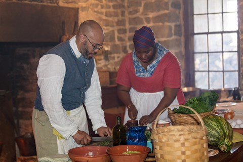 A man and woman portray enslaved cooks preparing food in a restored 1800s kitchen.