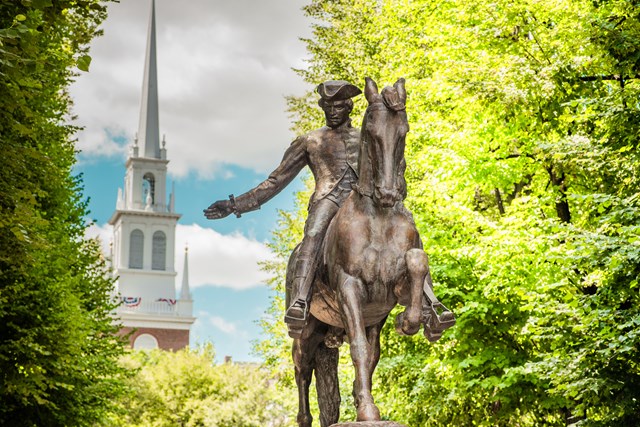 A bronze statue of Paul Revere riding a horse in front of the white steeple of Old North Church