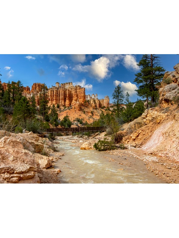 A creek meanders through red rocks with red rock formations in the background.