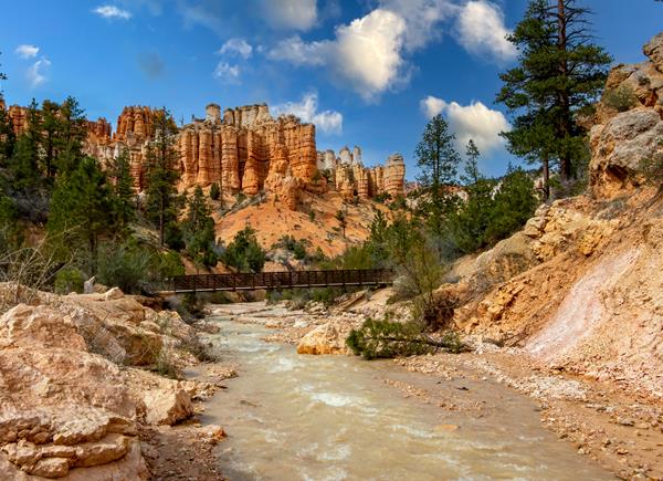 A creek meanders through red rocks with red rock formations in the background.
