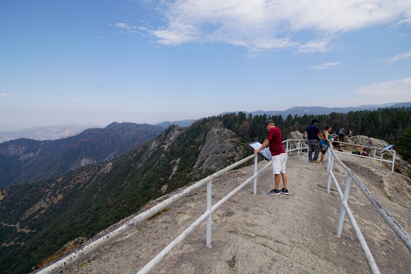 Protective railings sit atop a granite dome with many mountains in the distance