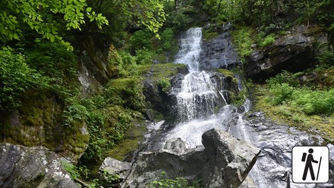 Waterfall that starts thin and fans out at the bottom. Boulders near base and vegetation on sides.