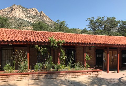 Single story adobe brick building with a red tile roof, Montezuma Peak is visible in the background.