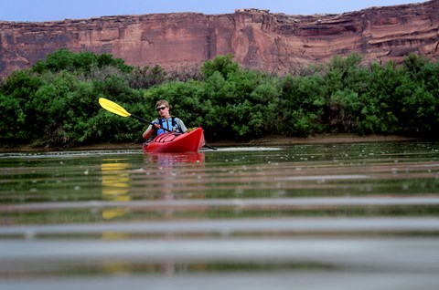 A kayaker floats atop still water at the bottom of a lush canyon.