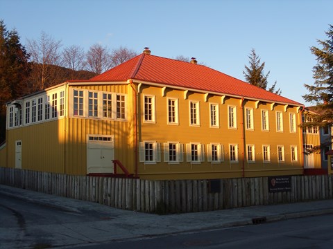 A two story yellow building with a red roof. A fence surrounds the building.