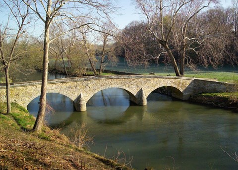 Three-arch stone bridge crossing Antietam Creek, bare trees and a cannon on the far grassy bank