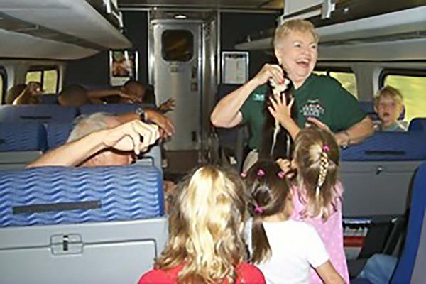 A woman in a green shirt holds up an animal pelt. Several people are gathered around looking at her.