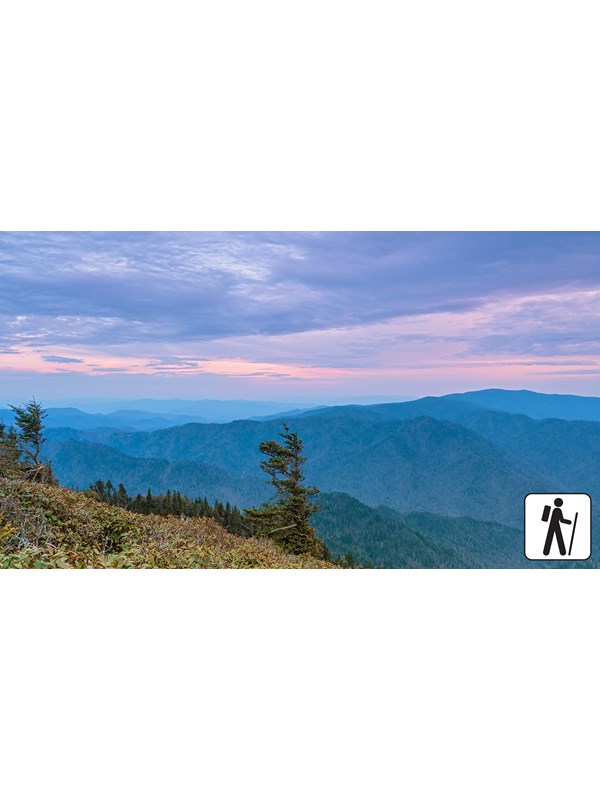 Sweeping mountain views below a pink and purple sky. Hiker icon in corner.