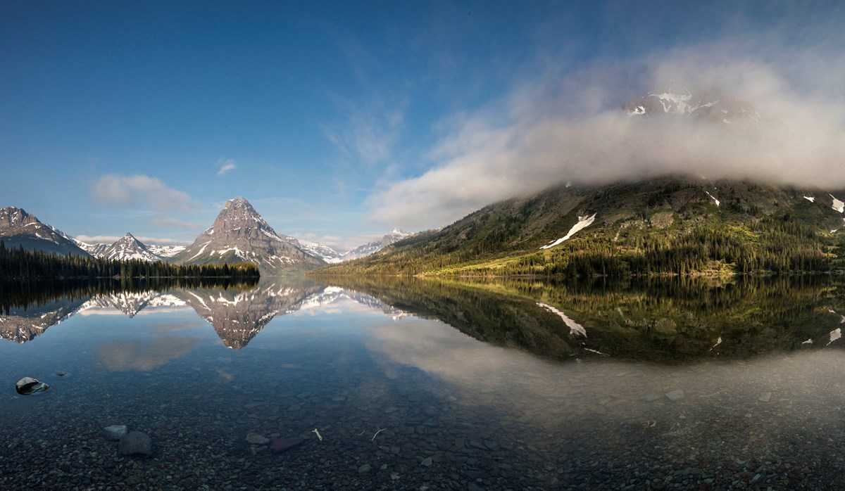 Snow-speckled mountains reflected into a calm lake.
