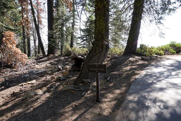 A metal sign stands next to a partially shade covered asphalt trail.