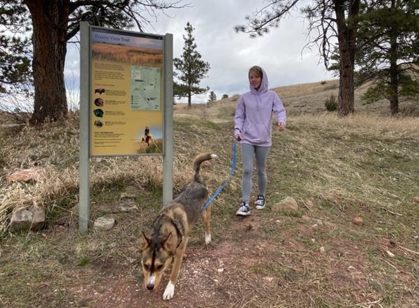 A visitor walks their dog with the Prairie Vista trailhead sign in the background.