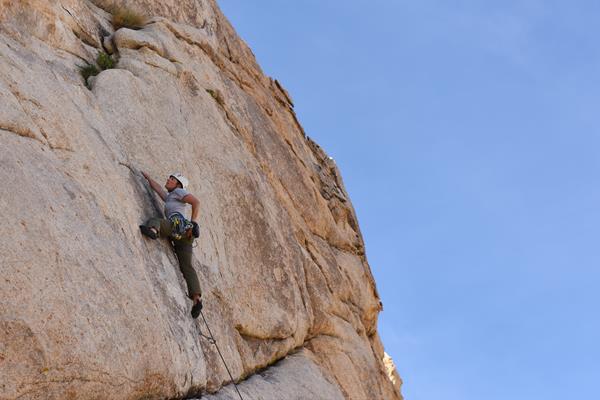 A rock climber making their way up a large tan rock face.