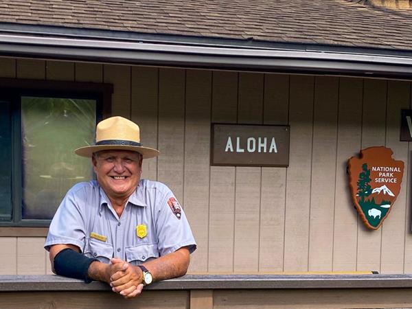 Ranger in flat hat stands in front of "aloha" sign