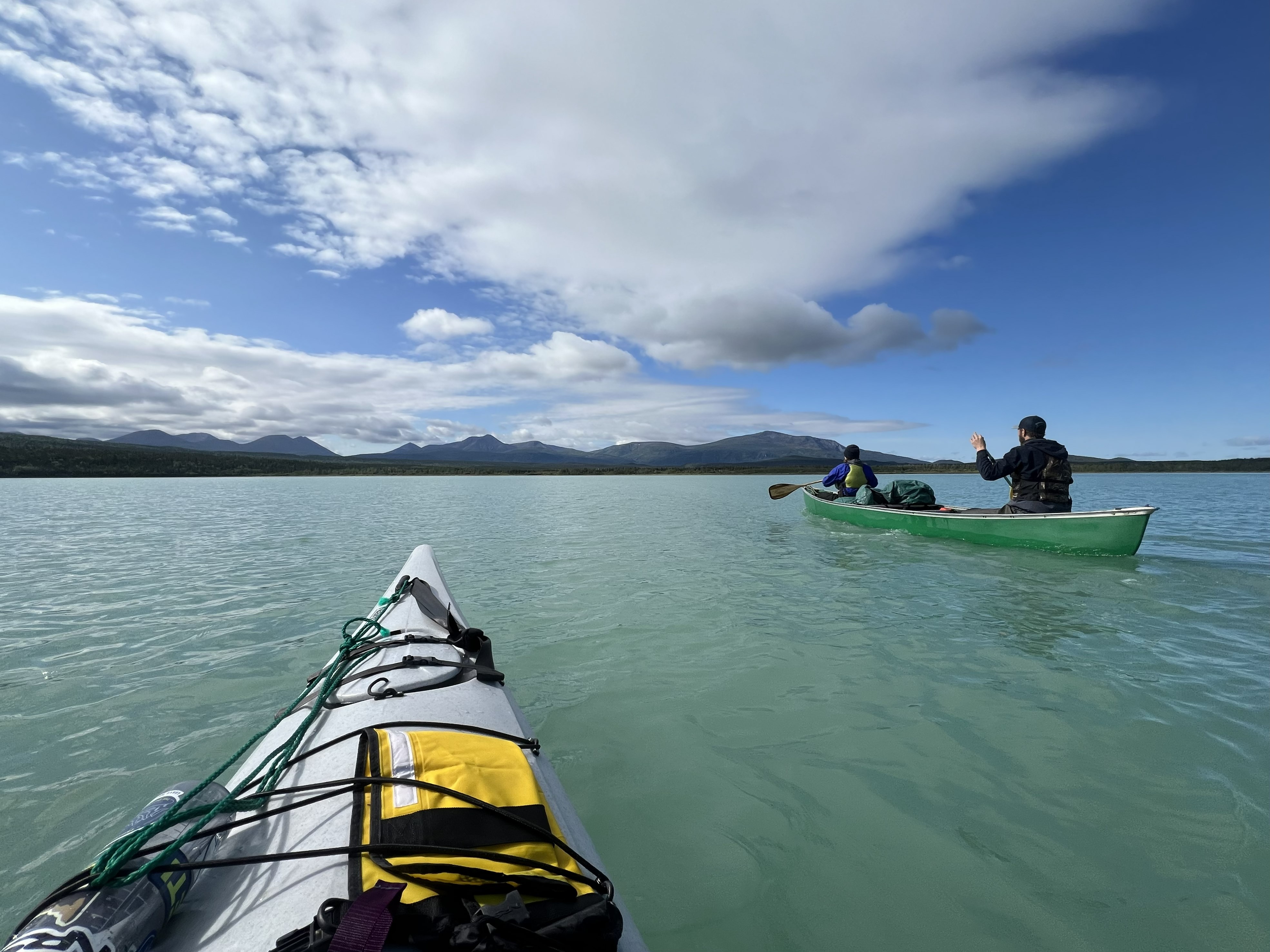 two boats glide through aqua waters toward a mountain range.
