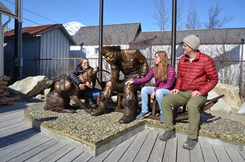 Three visitors sat next to a bronze statue of a gold prospector and his dog