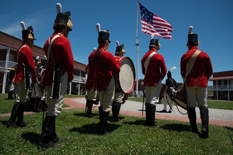 A group of living historians stand in the fort with the large garrison flag flying in the background