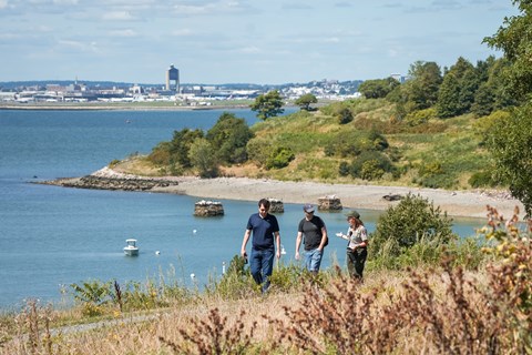 A ranger walks along a gravel path on an island talking to two other people