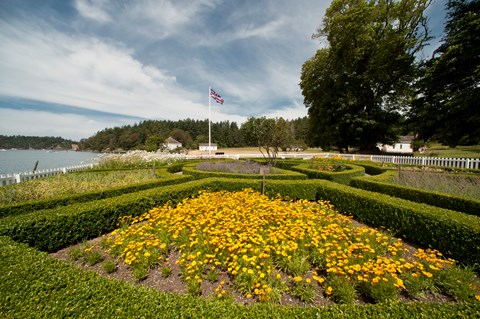 A formal garden with flowers and manicured hedges in front of historic English military buildings.