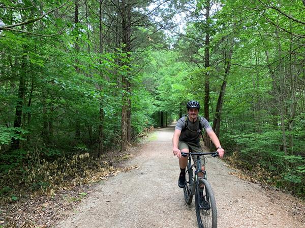 A young man rides a bike alone on a gravel trail.