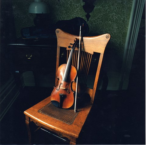 Violin and bow rests against wooden chair.