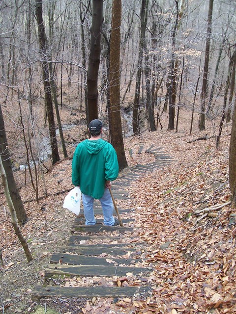 Image of hiker descending steep trail with staircase of wooden ties