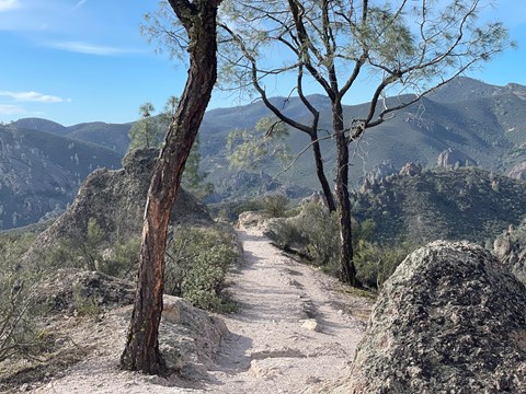 Rocky dirt trail on a mountain top with rolling mountains seen in the distance