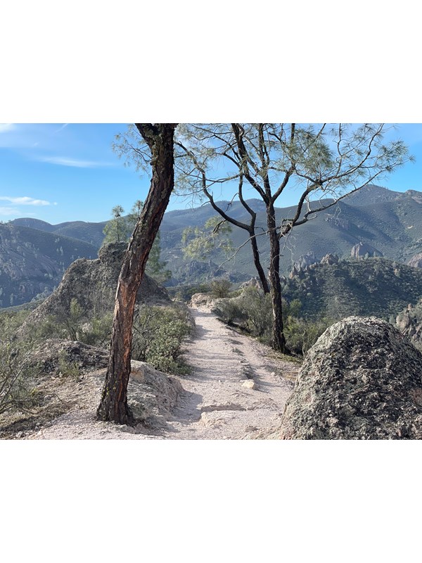 Rocky dirt trail on a mountain top with rolling mountains seen in the distance