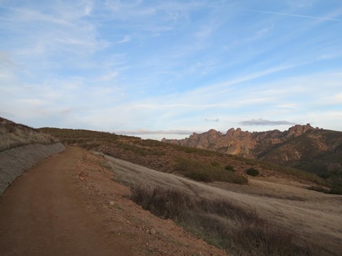 Hard pack dirt trail winding around hillside, large rock spires appearing in the distance.