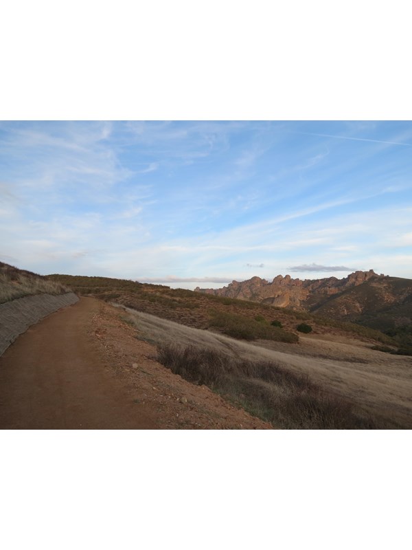 Hard pack dirt trail winding around hillside, large rock spires appearing in the distance.
