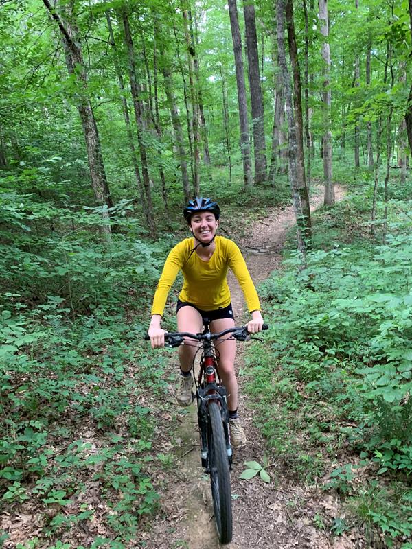 A young woman riding down a narrow trail on a mountain bike.