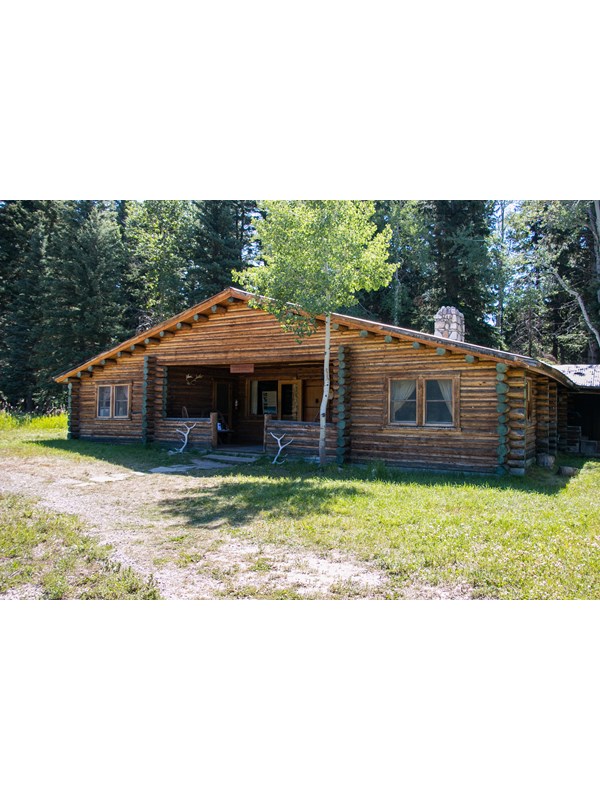 A brown, log cabin building with a river stone chimney and elk antlers resting on the front porch.