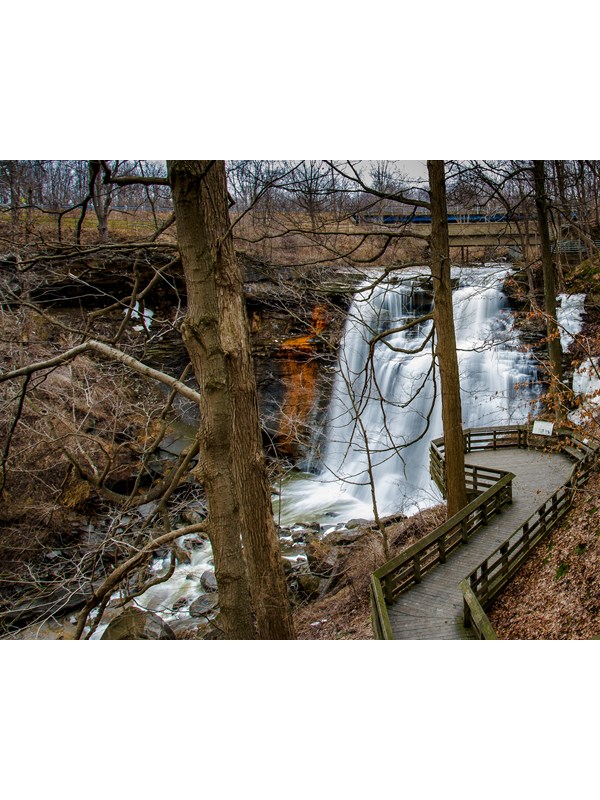 View down through bare trees at a deck overlooking a waterfall cascading into a gorge.