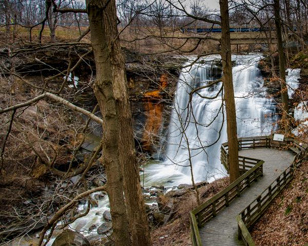 View down through bare trees at a deck overlooking a waterfall cascading into a gorge.