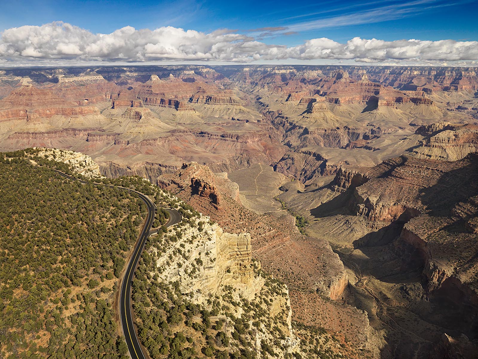 A paved scenic road in a forested area on the edge of a mile deep canyon filled with colorful peaks