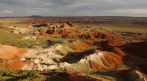 Red badland topography with highlights of sunlight under a cloudy sky.