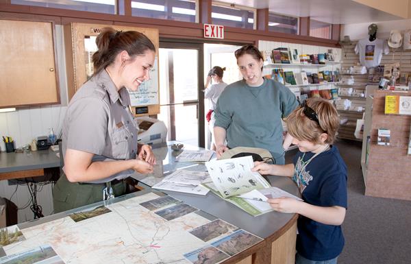 A female ranger reviews a young boy's junior ranger booklet, with mom watching from the side.