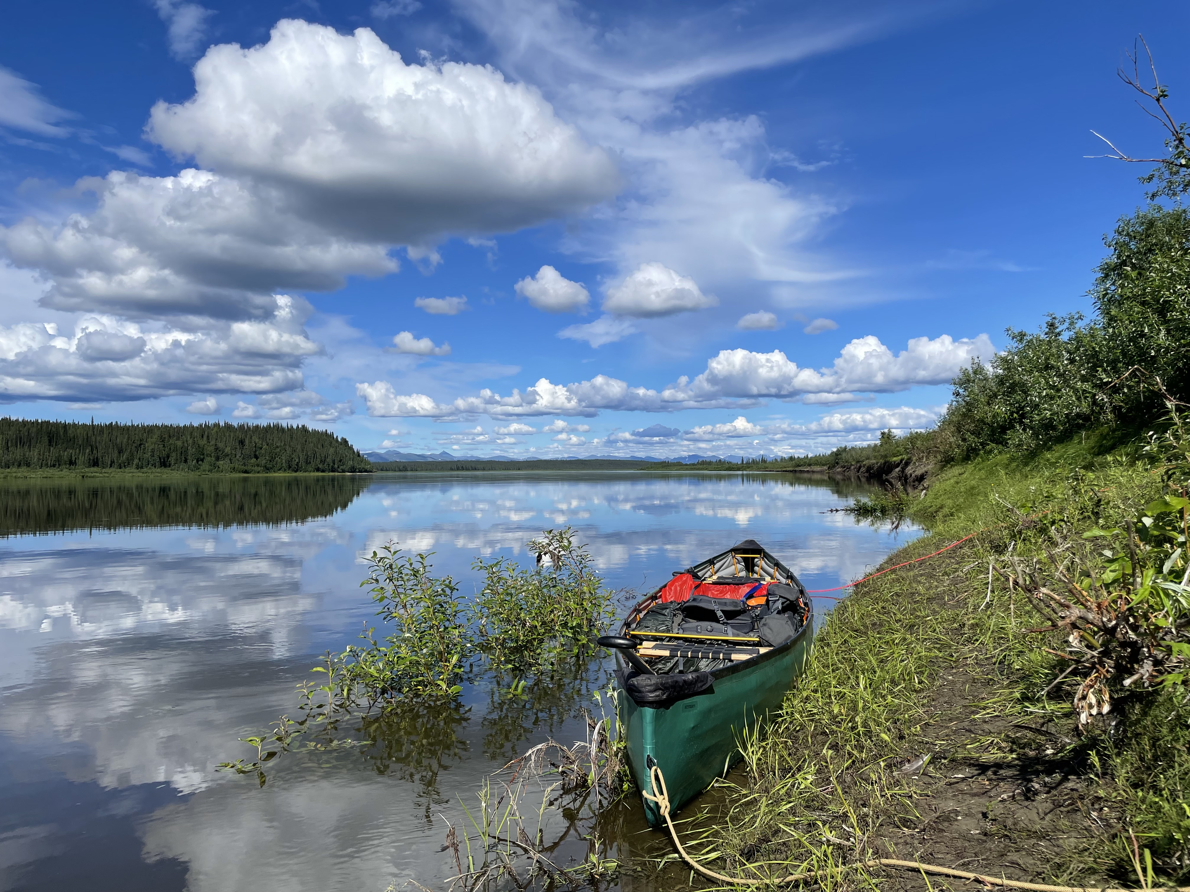 A green pack canoe is tied to the bank of the broad Kobuk River.
