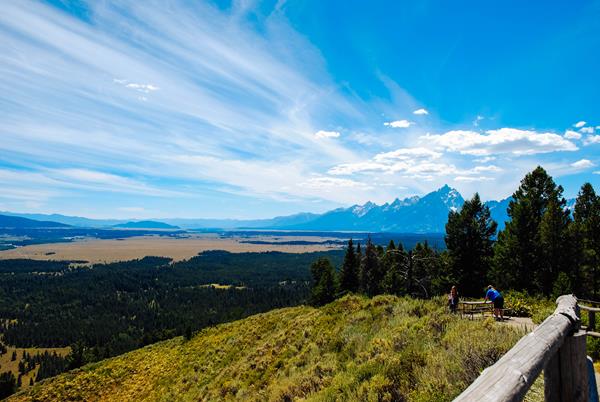 People stand on a hillside with mountains in the distance and steaks of clouds.