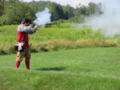 Demonstrator in period clothing firing a flintlock musket.