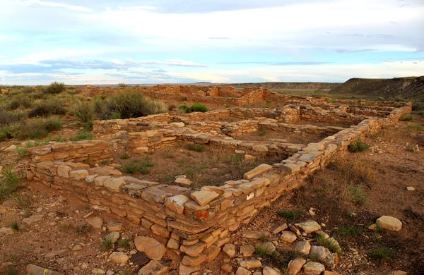 Puerco Pueblo masonry walls just after sunset with a partly cloudy sky, mesa in the background.