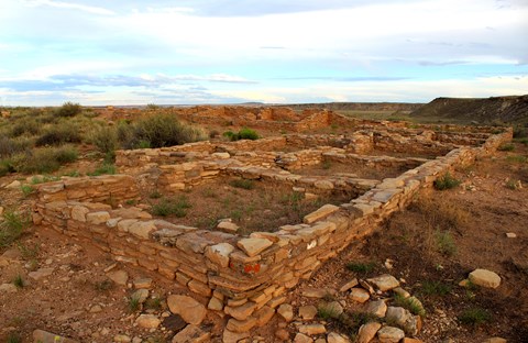 Masonry walls of Puerco Pueblo just after sunset, with a mesa and partly cloudy sky behind.