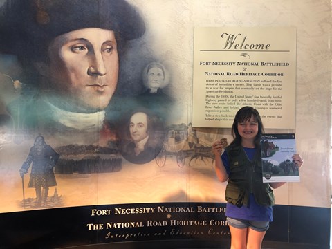 Girl holding a Fort Necessity Junior Ranger activity book and badge