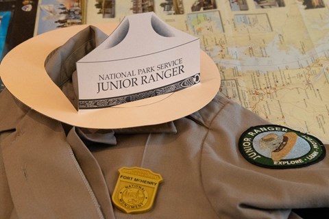 A shirt with a junior ranger patch, badge, and hat sitting on top of it.