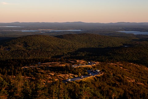 Sun rises over cars driving a mountain landscape with coastal bay in the background.
