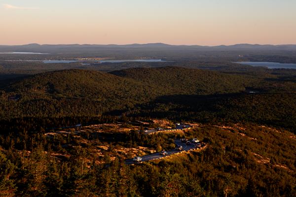 Sun rises over cars driving a mountain landscape with coastal bay in the background.